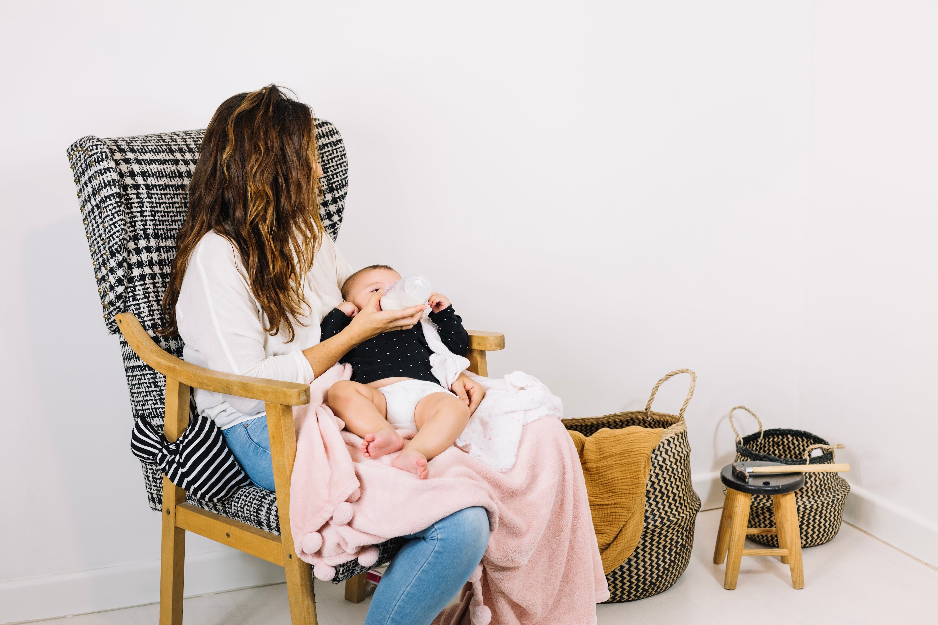 mother bottle feeds infant in chair